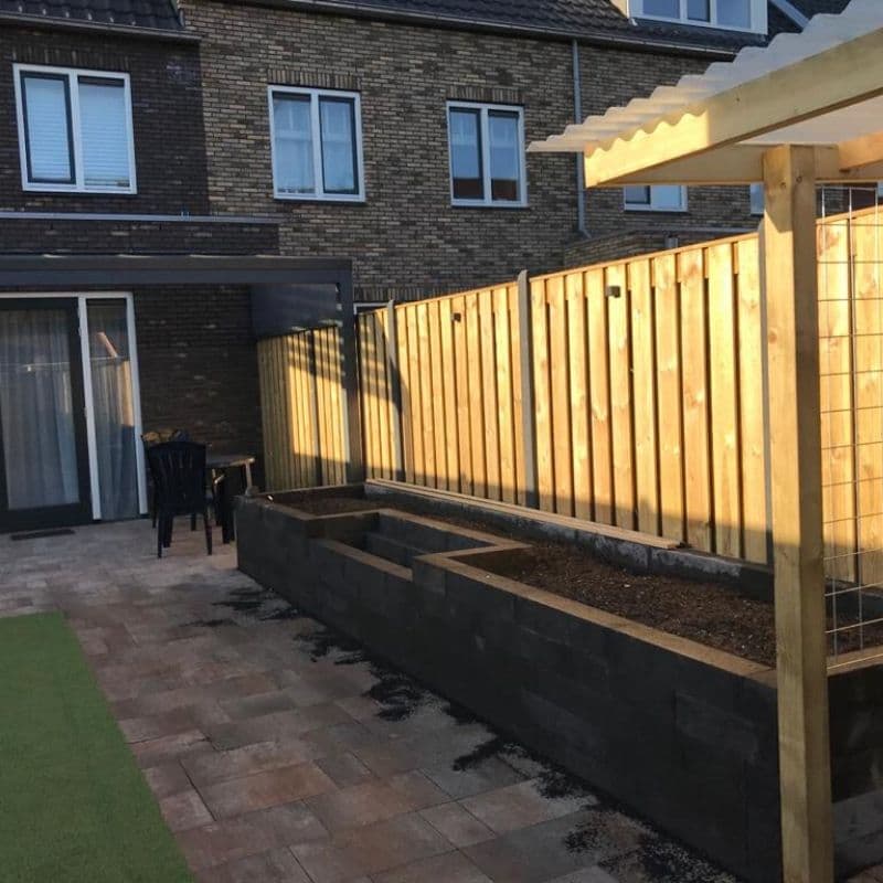 Verlichte houten schutting langs een terras met plantenbak